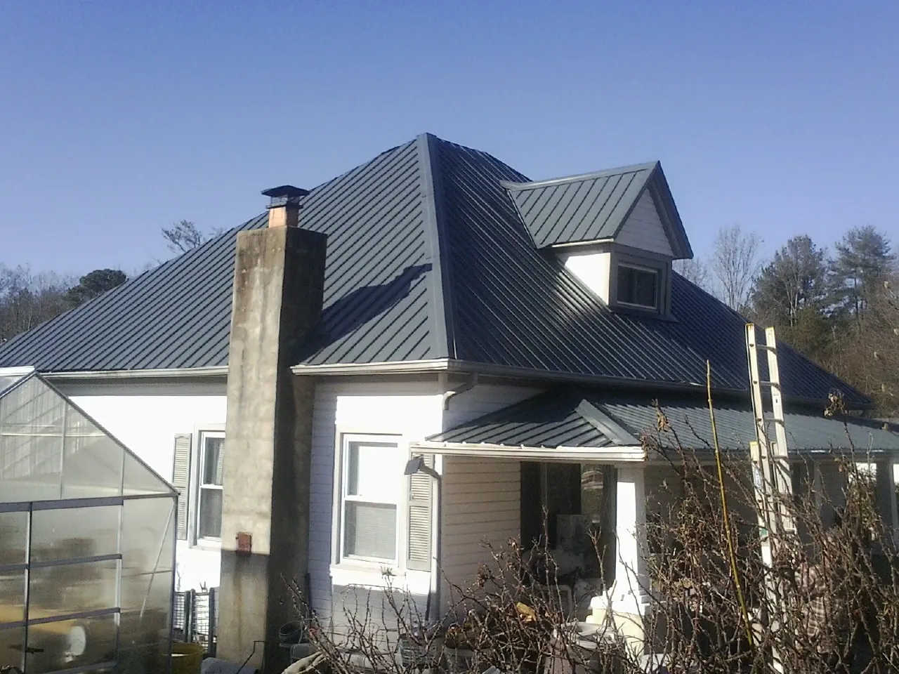 Dark blue standing seam metal roof on a white farmhouse with dormer — Slate & Tile Roof Repair by Roofing Brothers in Lavonia