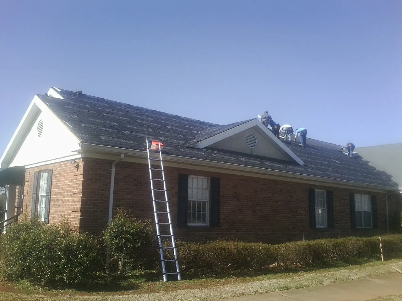 Crew tearing shingles off a brick ranch roof with a ladder set — Emergency Roof Repair work by our crew in Lavonia