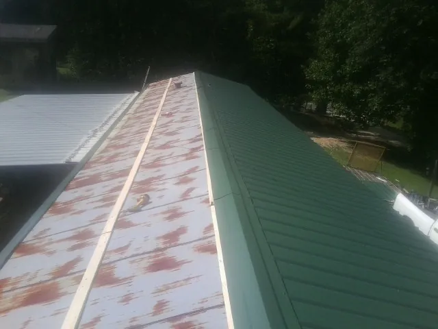 Old rusted panels beside newly installed green metal roofing — Wind Damage Roof Repair by Roofing Brothers in Lavonia