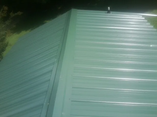 New green metal panels meeting at the ridge of a roof — Flat Roof Repair work by our crew in Lavonia