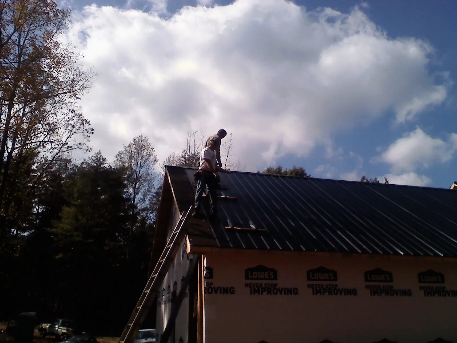 Roofer fastening dark metal panels high against a cloudy sky, from a Roof Inspection job in Lavonia