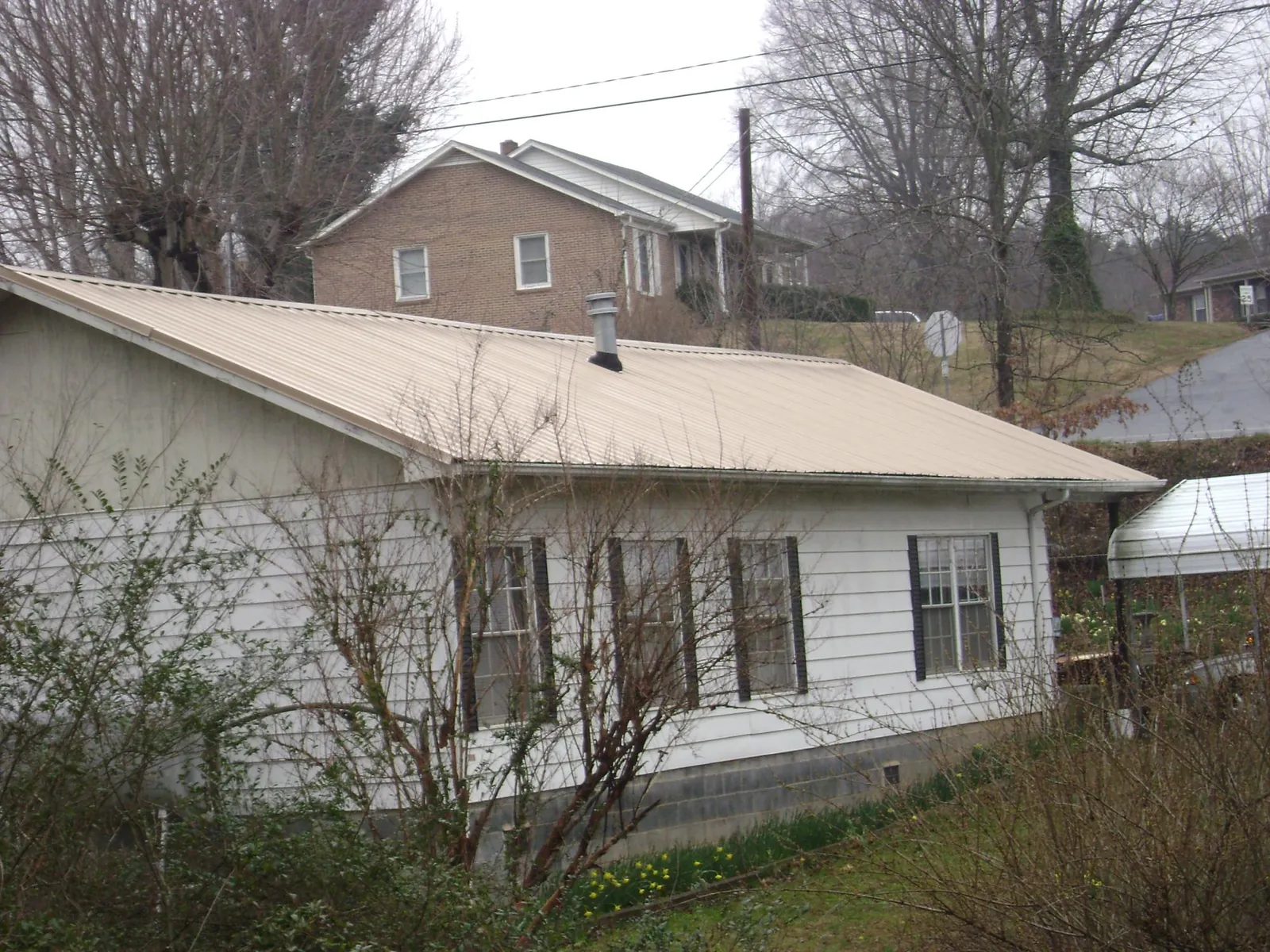 Tan metal roof on a white sided house set into a hillside — Commercial Roofing by Roofing Brothers in Lavonia